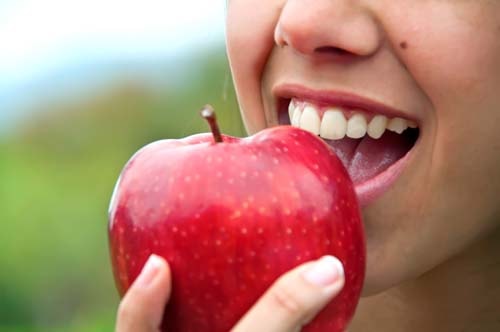 Bildet viser en kvinne som holder et eple mot munnen. Din tannhelse er avhengig av hvor bra du tar hånd om tennene. 